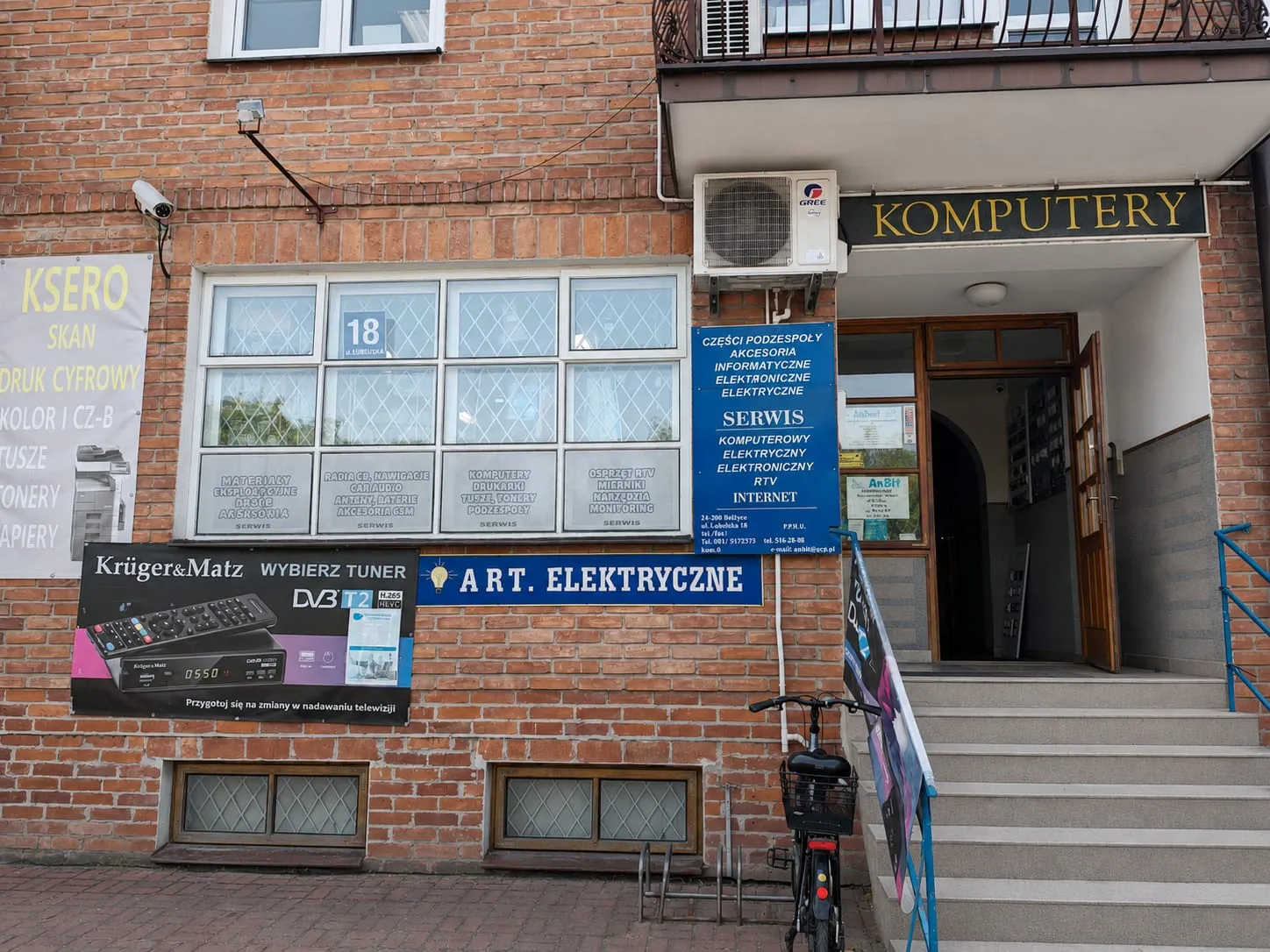 Wejście do sklepu AnBit przy ul. Lubelskiej 18 w Bełżycach — szyld Komputery nad drzwiami, tablice: Serwis, Art. Elektryczne, Ksero.