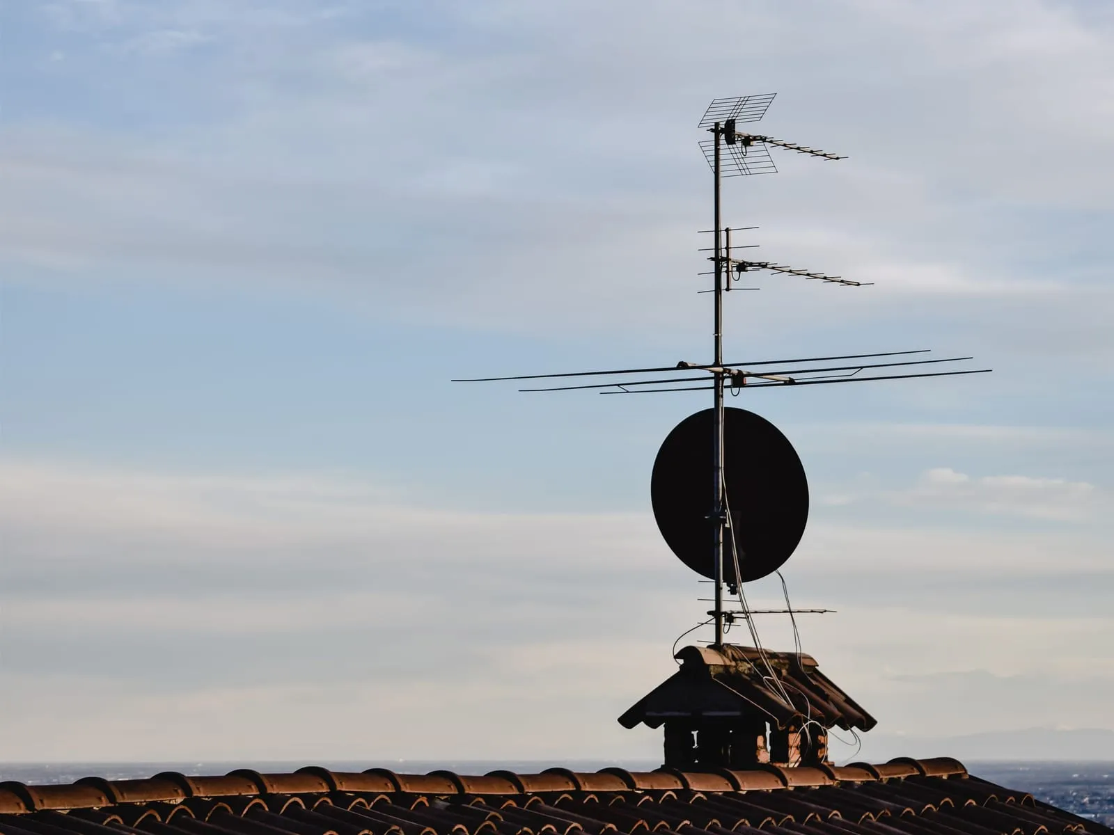 Antena naziemna DVB-T i talerz satelitarny na dachu domu na tle nieba